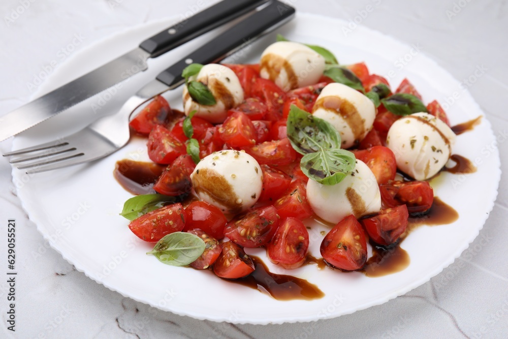 Tasty salad Caprese with tomatoes, mozzarella balls, basil and cutlery on white table, closeup Tasty salad Caprese with tomatoes, mozzarella balls, basil and cutlery on white table, closeup