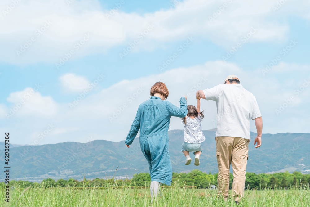 公園を手を繋いでジャンプしながら歩く家族・親子・ファミリーの後ろ姿（子供・両親・旅行）
