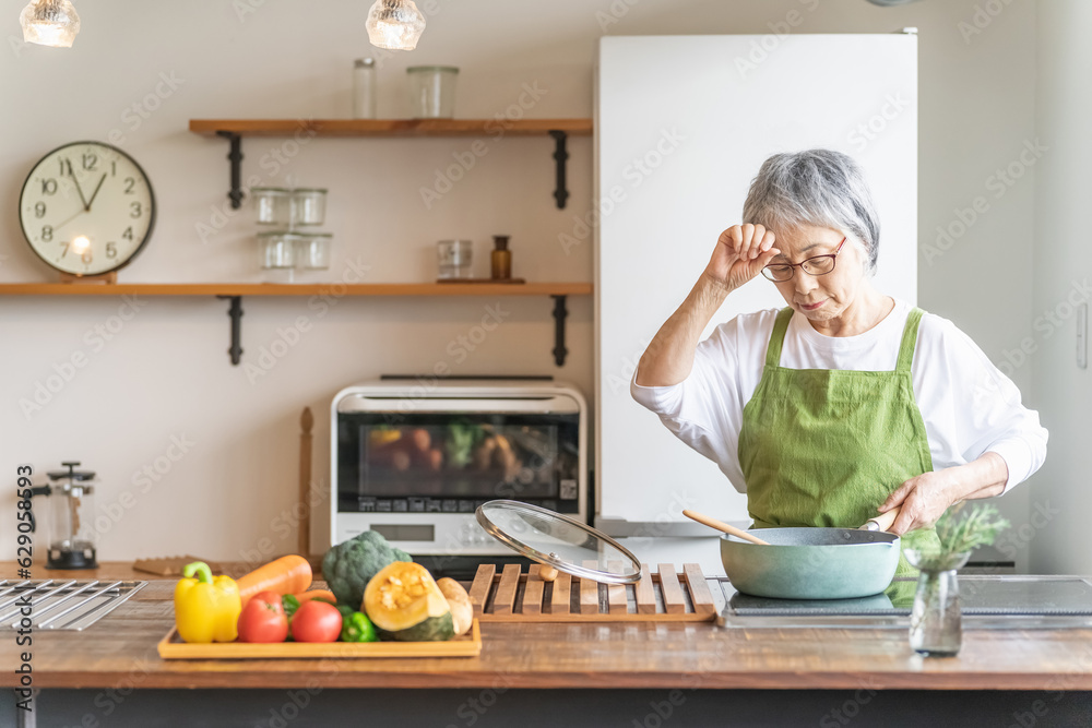 家のキッチンで料理を作るアジア人の高齢者女性（認知症・悩む）
