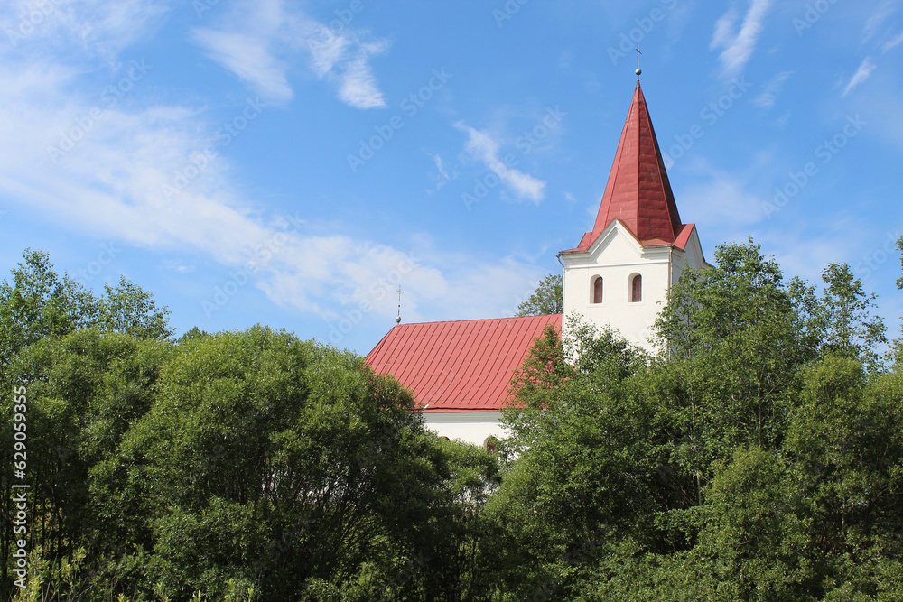 Lutheran church with a red steeple and trees in front of it in Eglaine, Latvia