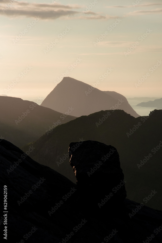 Mountain islands in Norwegian archipelago of Helgeland during sunset. Clouds forming on island mountain peaks at sea. Yellow sunset nordnorge. Dramatic contrast in Norway peaks. Smaltind, Luröy fjell