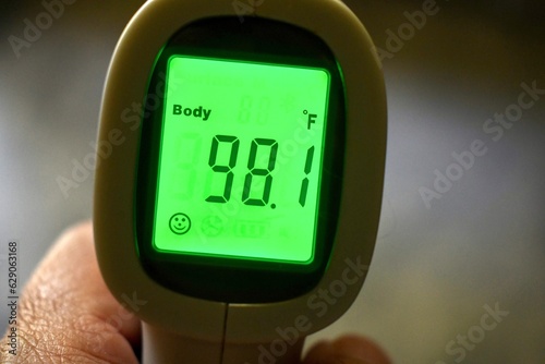 Hand holding a temporal thermometer with green digital reading in Fahrenheit 