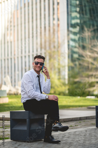 Urban business lifestyle: modern and young professional with white shirt and black tie using a phone in business district