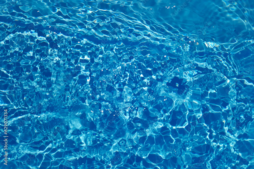 Obraz premium Blue water with ripples on the surface. Defocus blurred transparent blue colored clear calm water surface texture with splashes and bubbles. Water waves with shining pattern texture background.