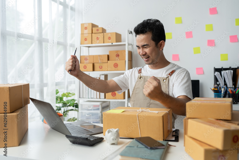 Young Asian businessman happy and excited after receiving new orders from SME customers. online marketing Entrepreneur packaging box, SME seller and independent online sales concept. Young Asian businessman happy and excited after receiving new orders from SME customers. online marketing Entrepreneur packaging box, SME seller and independent online sales concept.