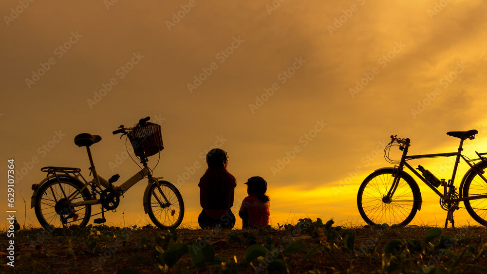 Obraz premium Silhouette biker lovely family sitting and talking at sunset over the ocean. Mom and daughter bicycling happy and relax on the beach. Lifestyle and Family Concept