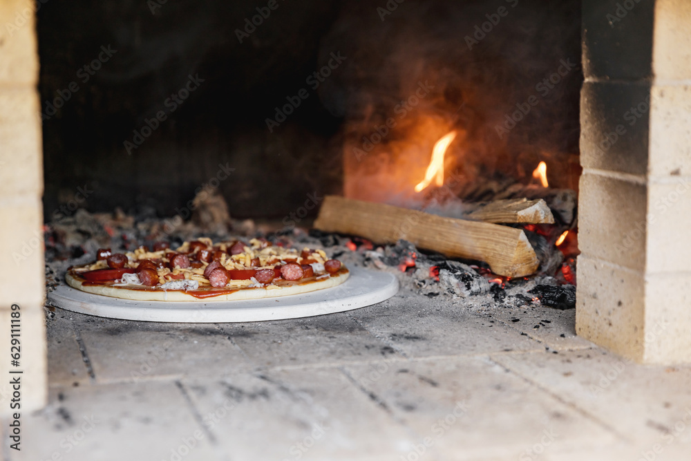 Pizza with sausages and tomatoes in a wood-burning oven against the background of firewood and fire. traditional italian food Pizza with sausages and tomatoes in a wood-burning oven against the background of firewood and fire. traditional italian food