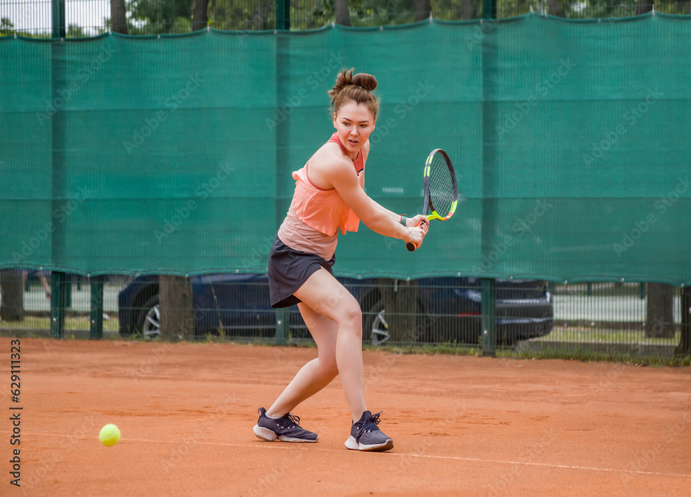 A young woman playing tennis hits backhand. Open ground.