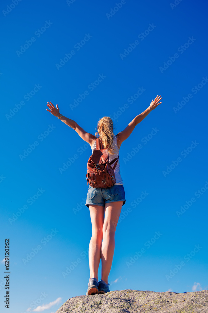 Woman standing on cliff with open arms against blue sky- freedom,  achievement,