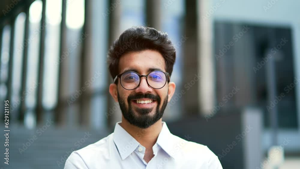 Close up portrait of a young businessman in a shirt and glasses smiling and looking at the camera. Handsome male posing standing on the street in front of an office building. Head shot of the manager