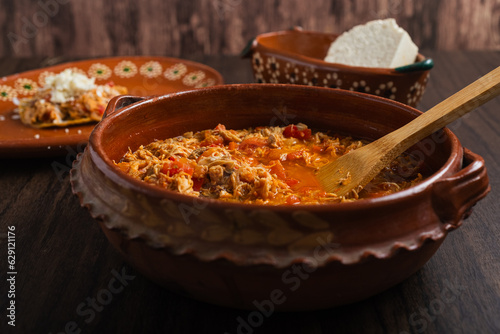 Authentic mexican chicken tinga, typical mexican food prepared in a clay pot on a wooden table.
