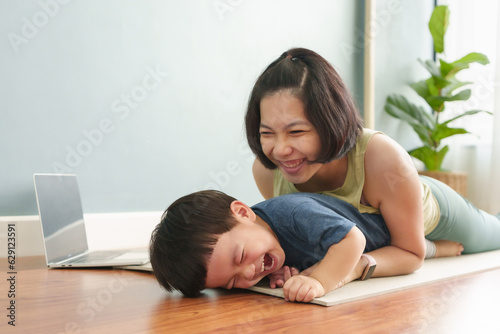Asian Japanese mother playing and hugging her adorable son on floor after practicing yoga exercise at home. Happy woman and little boy laughing and having Fun indoors.
