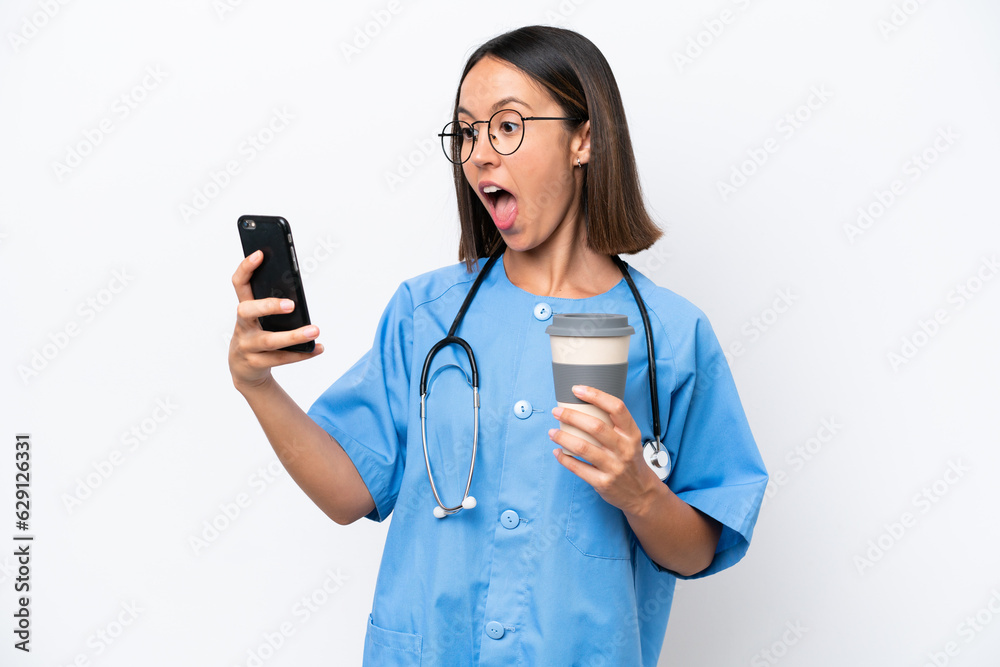 Young surgeon doctor woman isolated on white background holding coffee to take away and a mobile Young surgeon doctor woman isolated on white background holding coffee to take away and a mobile