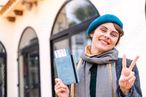 Brunette woman holding a passport at outdoors smiling and showing victory sign © luismolinero