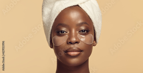 Face of black girl in hair towel with eye patches on skin.