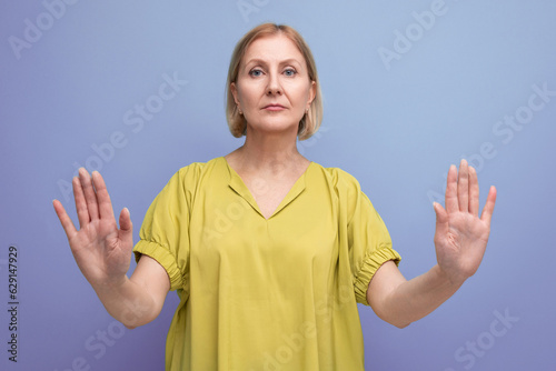 50s blonde woman in yellow t-shirt showing stop gesture