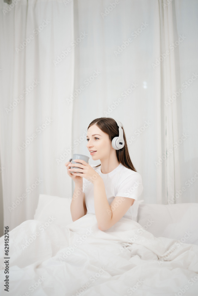 Beautiful woman has woken up on a white bed and holding coffee in the morning at home in morning Beautiful woman has woken up on a white bed and holding coffee in the morning at home in morning