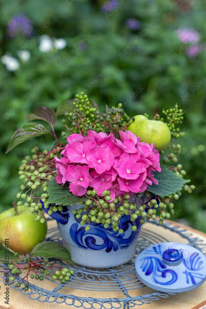florales Arrangement mit pink Hortensien-Blüten, Holunder-Beeren und Äpfeln