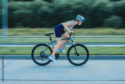 sports girl in a bicycle helmet and glasses rides a bicycle photo in motion, blurred background