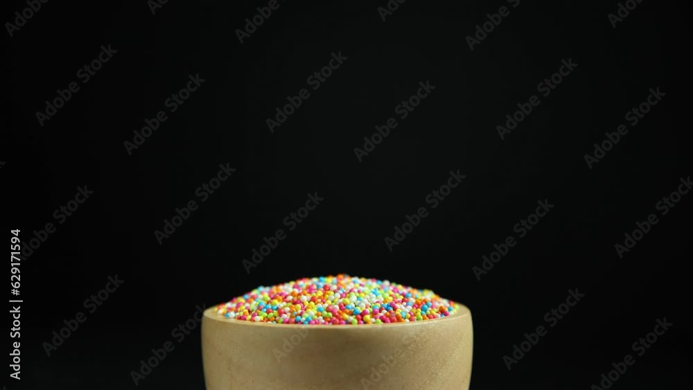 Sprinkle the wooden cup, rainbow, colorful sweets in the wooden cup, rotate in slow motion. Isolated on black background Sprinkle the wooden cup, rainbow, colorful sweets in the wooden cup, rotate in slow motion. Isolated on black background