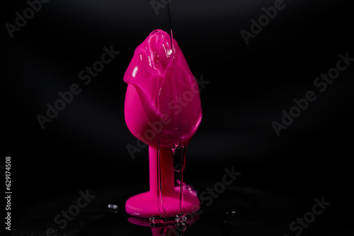 Pink anal plug in intimate lubricant on a black background. 
