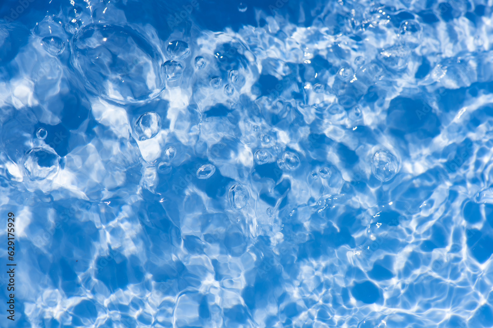 Obraz premium Blue water with ripples on the surface. Defocus blurred transparent blue colored clear calm water surface texture with splashes and bubbles. Water waves with shining pattern texture background.