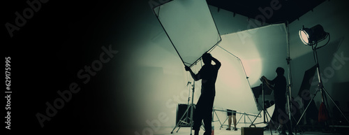 Silhouette of video production behind the scenes or B roll or making of TV commercial movie that film crew team lightman and cameraman working together with director in big studio with pro equipments photo