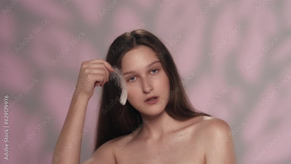 Beautiful young brunette model with long hair playing with small feather Beautiful young brunette model with long hair playing with small feather