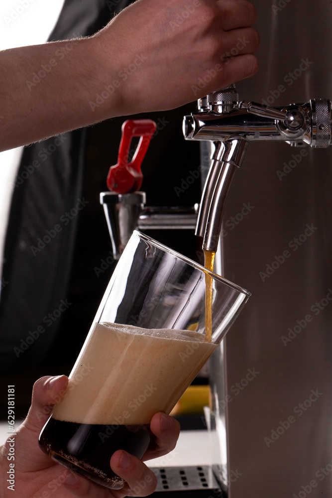 The bartender pours dark beer.