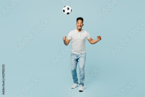 Full body sideways fun happy young man fan wear t-shirt cheer up support football sport team toss up soccer ball watch tv live stream do winner gesture isolated on plain pastel blue color background. photo