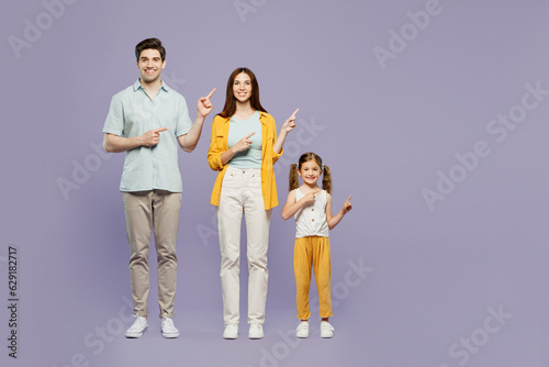 Full body young happy parents mom dad with child kid daughter girl 6 years old wear blue yellow casual clothes point index finger aside on area isolated on plain purple background. Family day concept.