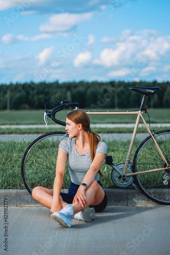 a girl sits and rests on the side of the road near a vintage bike