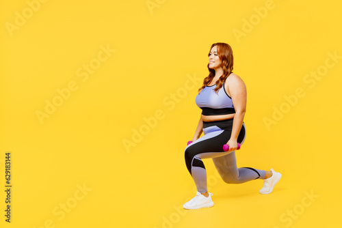 Full body side view young chubby plus size big fat fit woman wear blue top warm up training do squat lunges with dumbbells isolated on plain yellow background studio home gym. Workout sport concept.