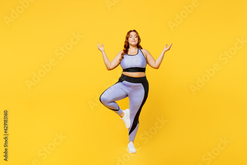 Fototapeta Naklejka Na Ścianę i Meble -  Full body young chubby plus size big fat fit woman wear blue top warm up train raise up hands leg in yoga om gesture meditate isolated on plain yellow background studio home gym Workout sport concept