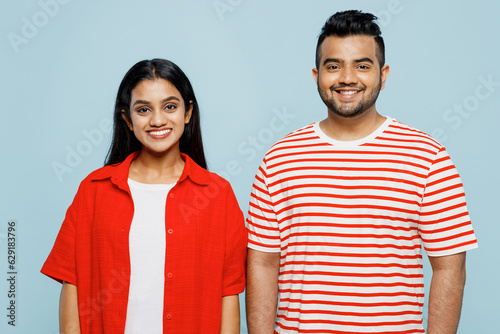 Young smiling happy cheerful positive fun couple two friends family Indian man woman wear red casual clothes t-shirts loking camera together isolated on pastel plain light blue cyan color background.