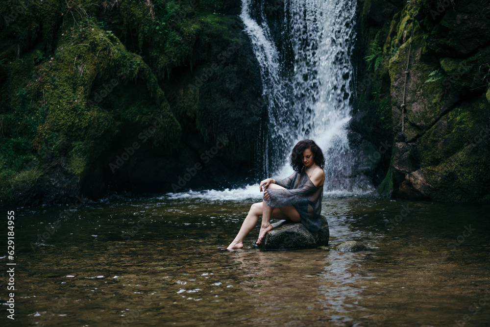 Fototapeta premium Beautiful young woman sitting on rock near mountain river in forest. High quality photo
