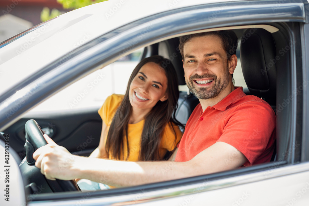Cheerful millennial couple travellers smiling from car window