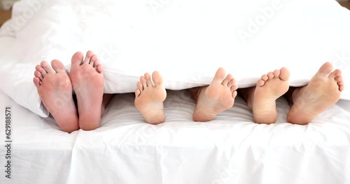 Female and two pairs of male legs lying under blanket at home 4k movie slow motion. Sexual fantasy threesome concept