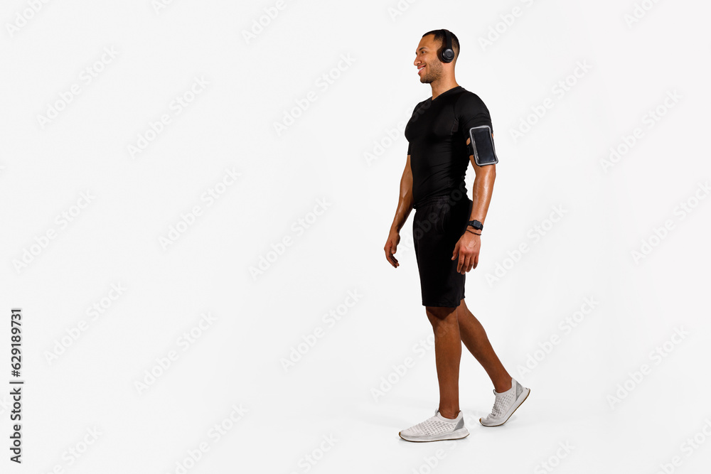 Fototapeta premium African Fitness Guy With Headphones Walking To Copy Space, Studio