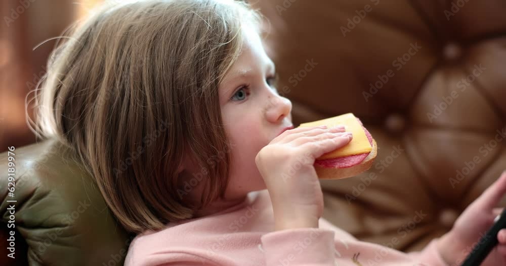 Child lying on sofa and eating delicious sandwich with sausage and cheese 4k movie slow motion. Proper nutrition in children concept Child lying on sofa and eating delicious sandwich with sausage and cheese 4k movie slow motion. Proper nutrition in children concept