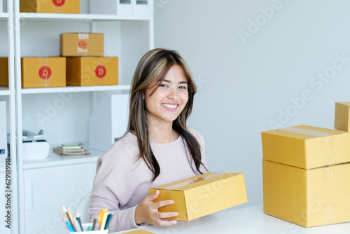Young asian small business owner holding prodect boxes while smiling and looking at camera, online shopping