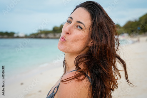 brunette-haired latina girl blowing a kiss on the beach