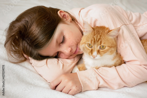 friendship between child and pet. A cute little girl is resting on the bed with her cat. Red Cat