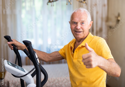 Mature man exercising on an elliptical machine and showing thumb up