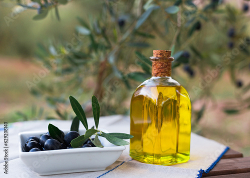 olive oil in a glass bottle and green olives on the background of olive branches in the garden
