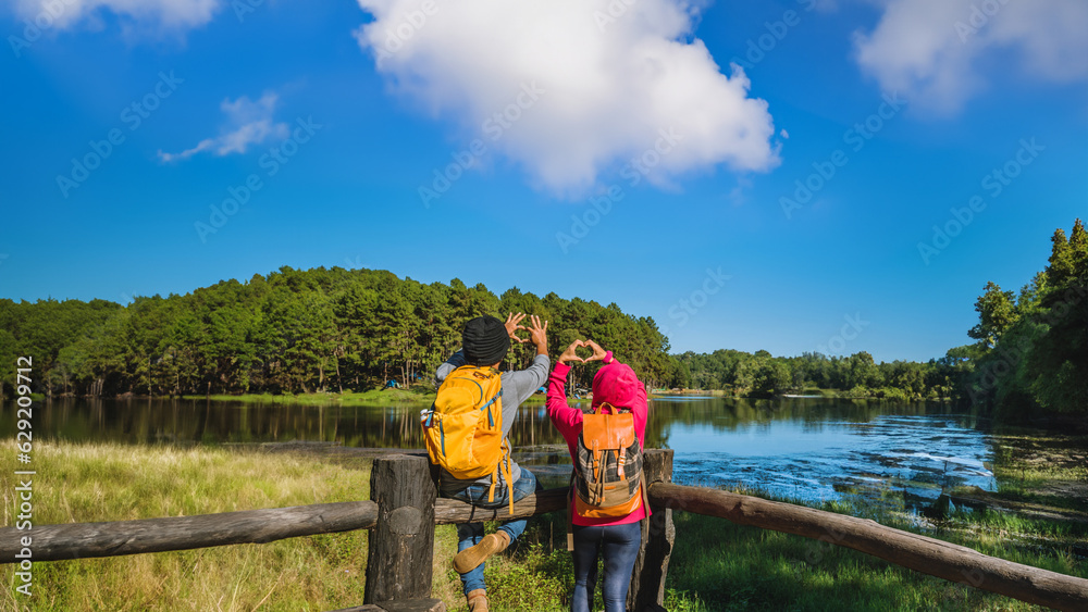 Couples travelers with backpack happy to relax on mountain, with lakes, beautiful ponds pine forests. couples raise their hands to make a heart shape. Happy and sweet love. Couples travelers with backpack happy to relax on mountain, with lakes, beautiful ponds pine forests. couples raise their hands to make a heart shape. Happy and sweet love.