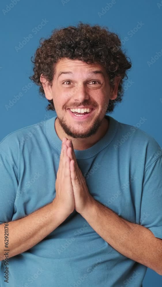Surprised man looking at camera with big eyes, clapping his hands, isolated on blue background in studio Surprised man looking at camera with big eyes, clapping his hands, isolated on blue background in studio