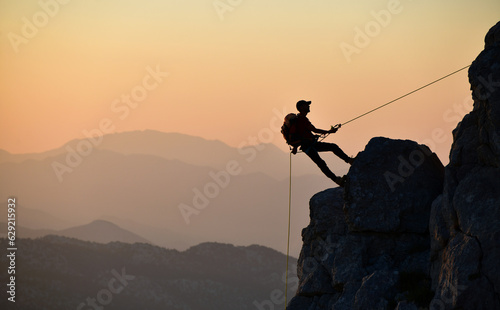 Silhouette of man climbing rock with rope