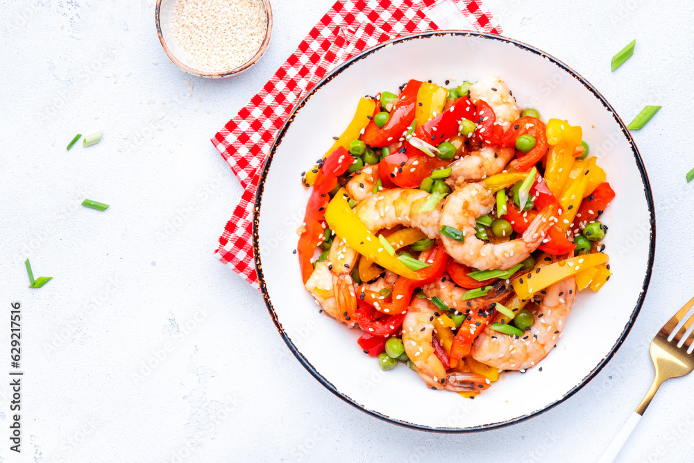 Stir fry shrimps, red paprika, green peas, chives and sesame seeds in ceramic bowl. Asian cuisine dish. White table background, top view Stir fry shrimps, red paprika, green peas, chives and sesame seeds in ceramic bowl. Asian cuisine dish. White table background, top view
