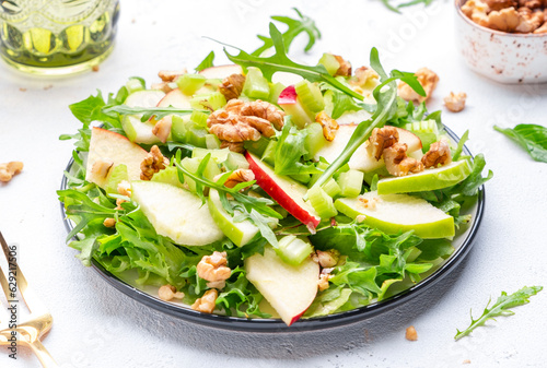 Waldorf salad with apples, green celery, lettuce, arugula and walnuts on plate, white background, top view